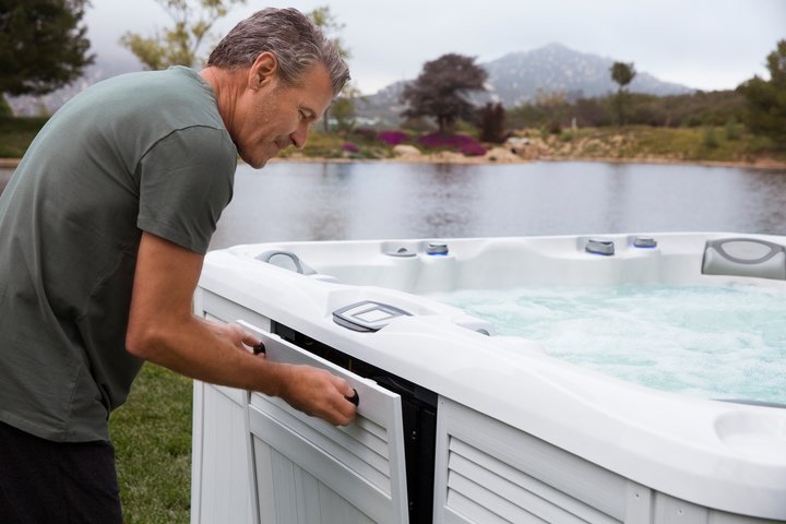man opening his hot tub access panel to perform hot tub maintenance